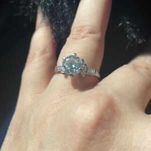 Silver band with fake diamond stone in middle and other stones on side.